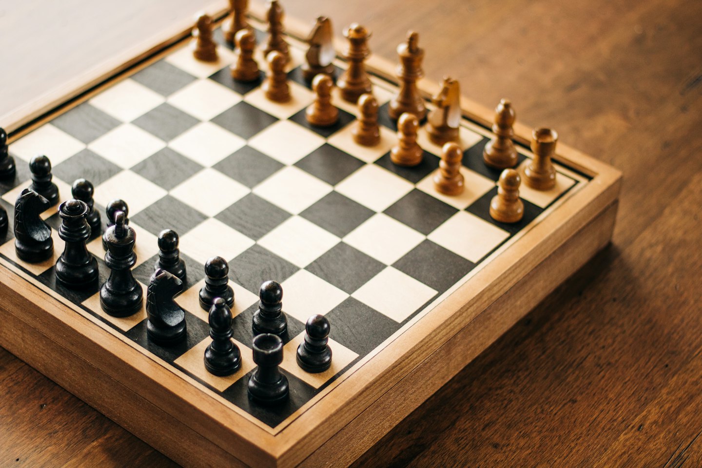 Wooden chessboard with pieces on a dark table.