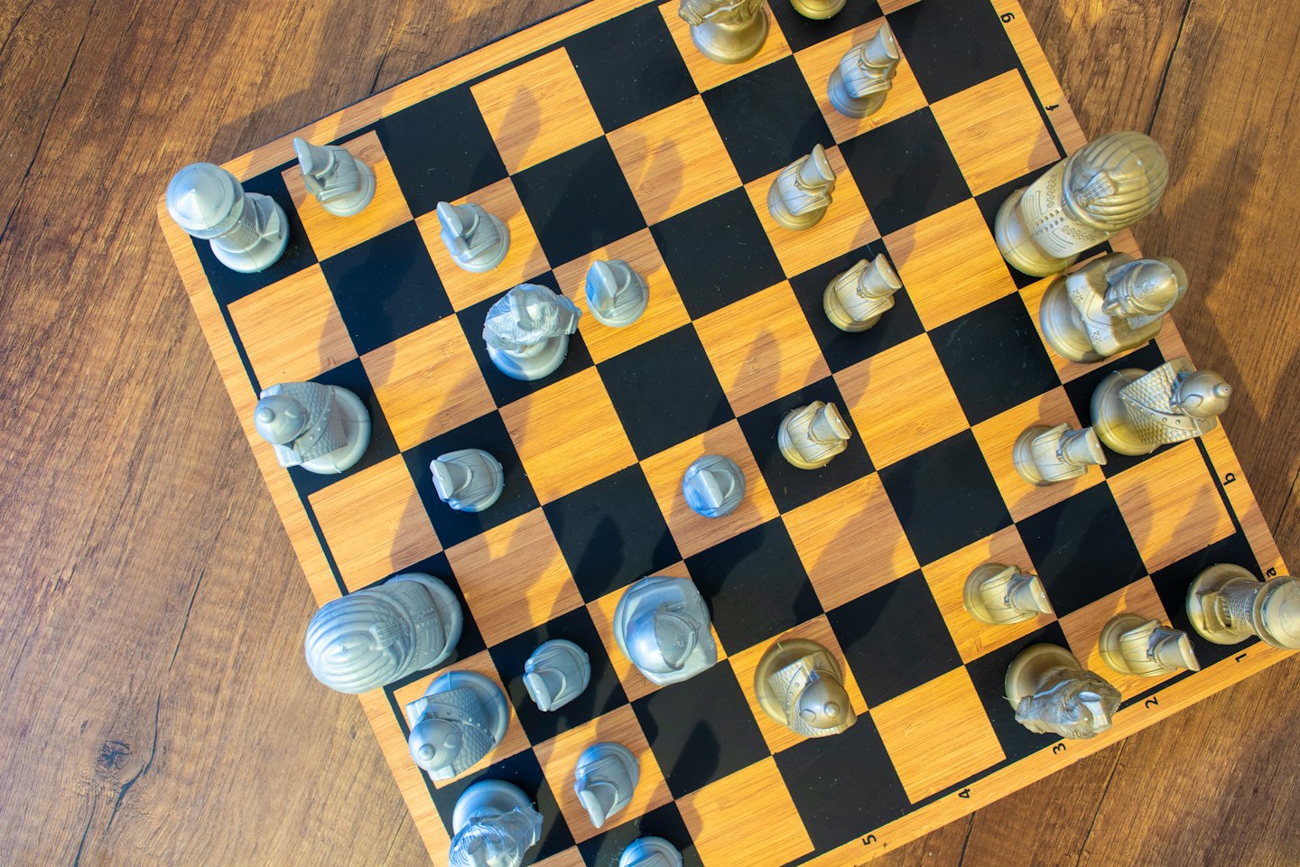 Gold and silver chess pieces sit on a wooden board.