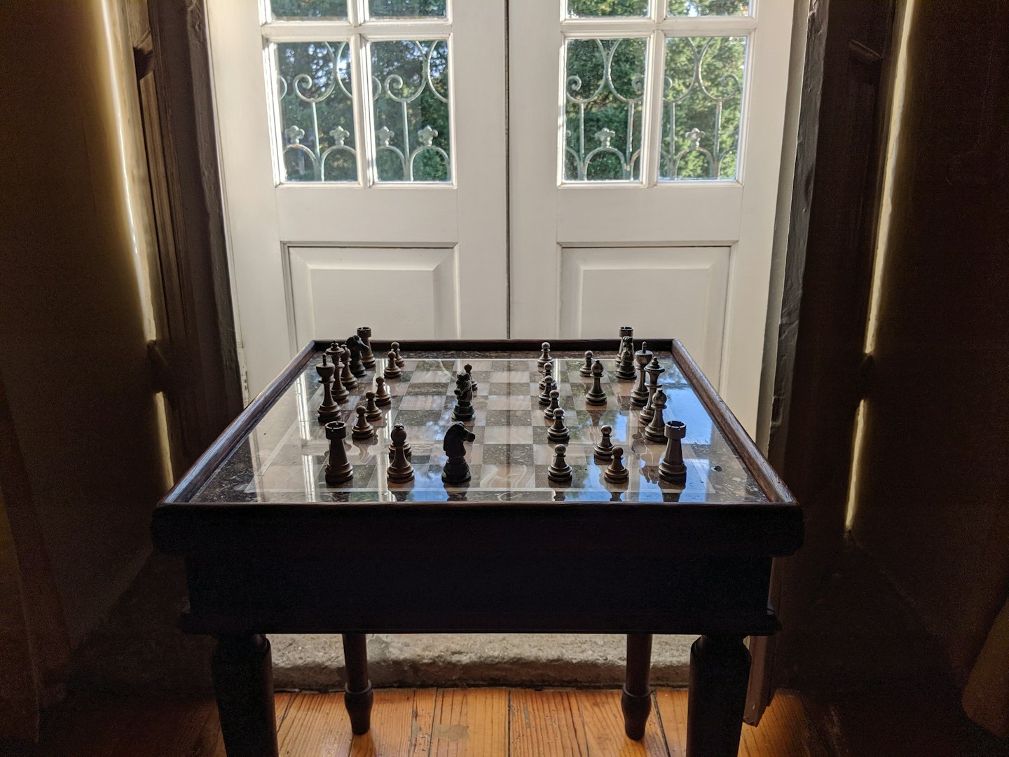 A chess set arranged on a wooden table near doors.