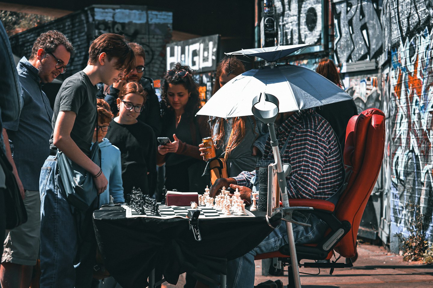 People watch a chess game on a sunny urban street.