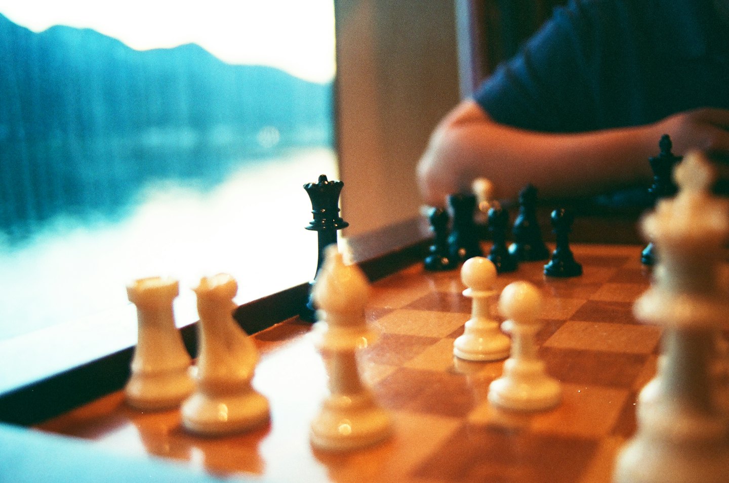 A person moves a black chess piece on a wooden board.