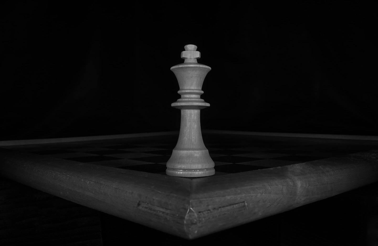 A white chess king piece stands on a wooden board.