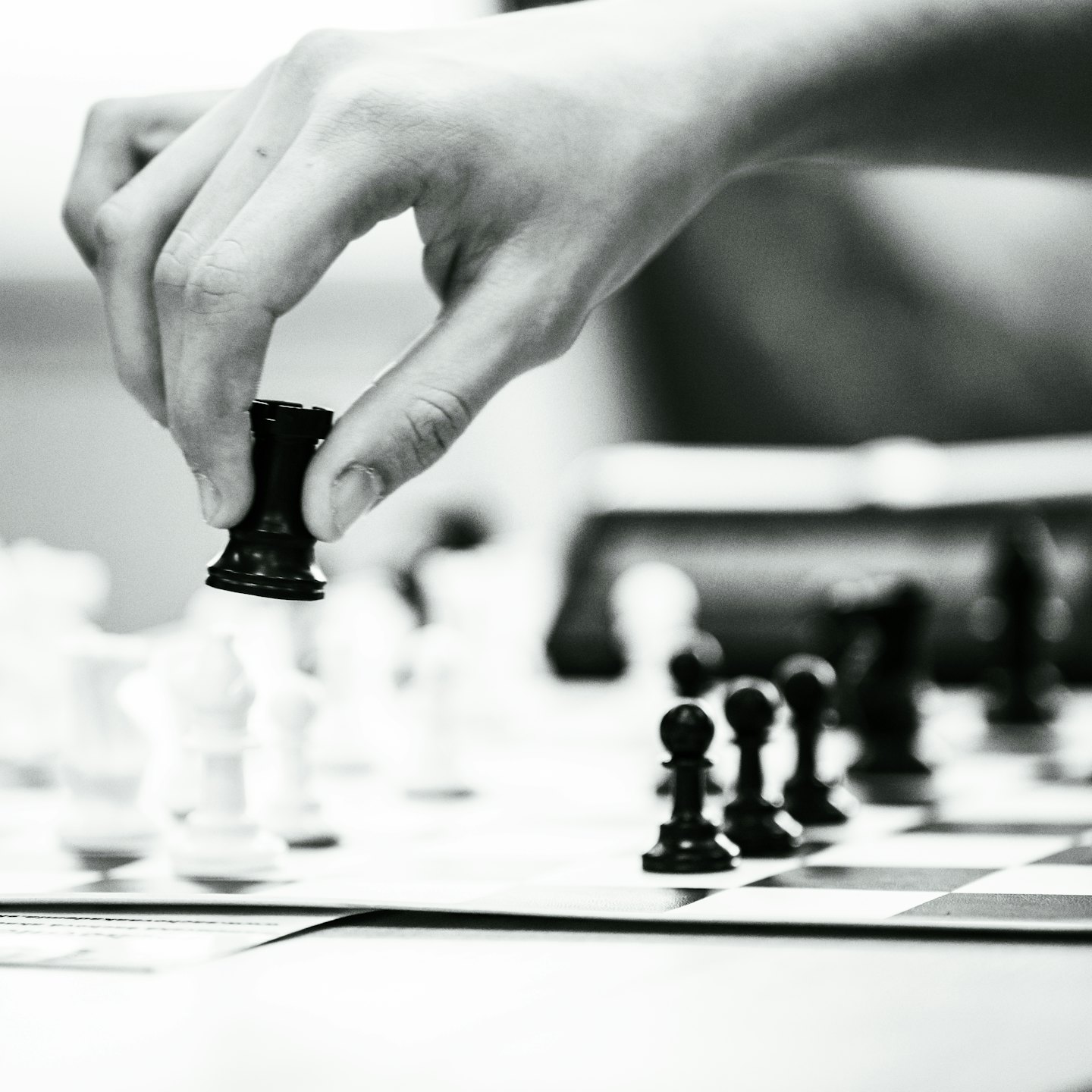 Hand moving a black rook chess piece across a checkered board.